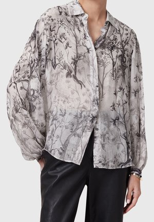 Semi-doorzichtige grijze blouse met zwarte bloem- en vogelpatronen, lange opgeblazen mouwen, knoopsluiting aan de voorkant, gecombineerd met zwarte leren broek.