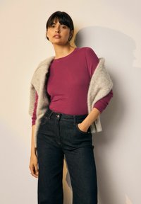 Hosszú ujjú magenta felső sötét, magas derekú farmerral párosítva, egy világosszürke textúrált sállal átdobva. Egyszerű, modern dizájn.