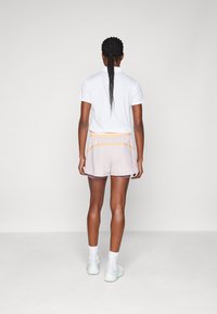 Fehér póló, világoslila nadrág narancssárga részletekkel, rugalmas derékkal, fehér zoknikkal és világoszöld sportcipőkkel párosítva.