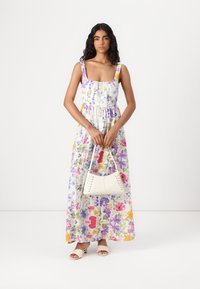 Robe maxi florale blanche avec des fleurs colorées ; présente un décolleté carré, une taille froncée et des bretelles réglables. Accompagnée d'un sac blanc.