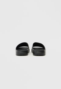 Black rubber sandals with a simple design, featuring a smooth texture and open-toe, backless style. Brand logo embossed on the side.