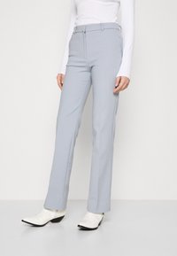 Jasnoniebieskie spodnie szyte na miarę z prostymi nogawkami, z paskiem na szlufkach i płaskim przodem. Noszone z białymi botkami za kostkę.