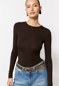 Kobieta ubrana w dopasowaną czarną bluzkę z długim rękawem, niebieskie jeansy wysokiego stanu i pasek w leopardzi wzór z okrągłą klamrą.