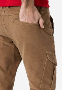 Bruine corduroy cargobroek met een zijzak en een gestructureerde afwerking, met zichtbare stiksels nabij de tailleband.