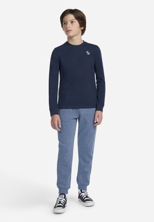 Chemise à manches longues bleu marine avec un petit logo blanc, associée à un pantalon de jogging bleu clair et des baskets noires avec des accents blancs. Design simple dans l'ensemble.