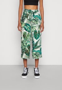 Spodnie culotte z zielonym wzorem liści na białym tle, z wiązanym pasem i luźnym krojem. Połączone z czarnymi trampkami za kostkę.