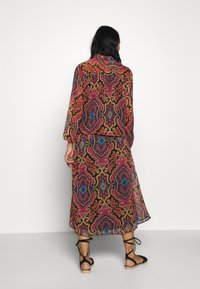 Robe longue imprimée avec un motif paisley coloré dans des nuances de rouge, bleu et or, en tissu transparent et fluide, avec une taille élastique.