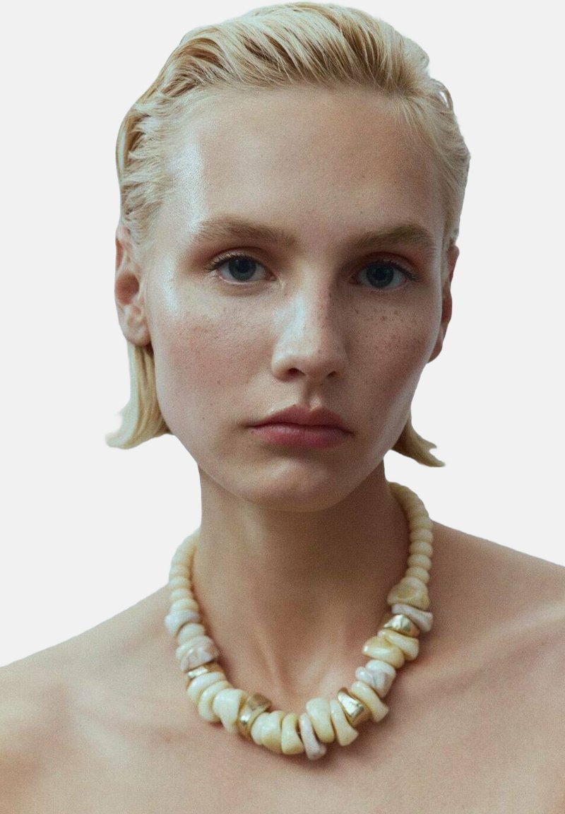 Collier perlé composé de perles blanc cassé, certaines texturées, entrecoupées d'accents dorés brillants. Fini lisse et formes arrondies.