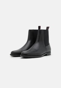 Bottes Chelsea en cuir noir avec panneaux latéraux élastiques, bout arrondi et petit talon, agrémentées de languettes de tirage contrastées. Texture lisse et design élégant.