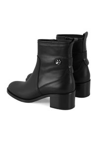 Bottes noires en cuir à la cheville avec un talon bloc modeste, fermeture éclair latérale et un accent en matériel circulaire sur le côté. Texture lisse et design élégant.