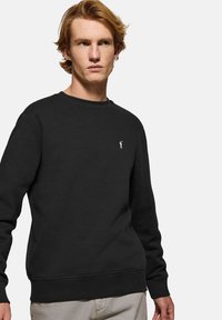 Svart sweatshirt med rundad halsringning, ribbade ärmslut och nederkant. Har en liten vit logotyp på bröstet. Tillverkad av ett mjukt tyg.