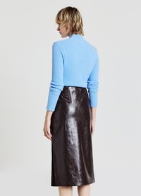 Hellblauer, strukturierter Pullover, kombiniert mit einem dunkelbraunen, glänzenden Leder-Midirock mit seitlichem Schlitz. Minimalistisches Design und figurbetonte Silhouette.