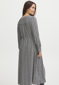 Juodai baltas raštuotas suknelė su bangos raštu, ilgomis rankovėmis ir susikaupusiu nugara, siekianti per vidurį blauzdos.