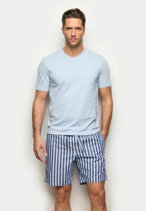 Uomo in piedi che indossa una T-shirt a maniche corte azzurra e pantaloncini con righe verticali blu e bianche con coulisse.
