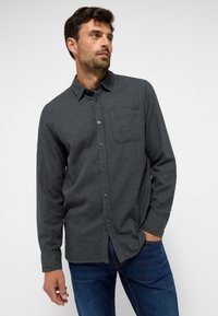 Dunkelgraues Hemd mit Knopfleiste aus einem strukturierten Stoff, mit einer Brusttasche, klassischem Kragen und langen Ärmeln, kombiniert mit blauen Jeans.