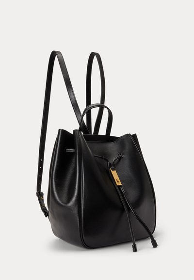 Μαύρο δερμάτινο σακίδιο τύπου κουβά με διπλούς ιμάντες ώμων, χειρολαβή στην κορυφή και κλείσιμο με κορδόνι με χρυσή λεπτομέρεια σε απλό φόντο.