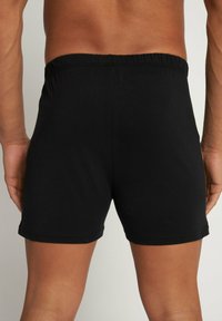 Zwarte katoen boxershorts met een elastische tailleband, met een gladde, rekbare textuur en afgewerkte zomen. Geen zichtbare patronen of logo's.