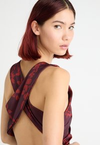 Robe bordeaux avec un motif floral rouge, présentant un dos ouvert et des bretelles croisées. Texture lisse avec une coupe ajustée.