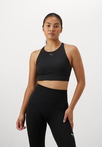 Svart sportsbh med høy hals og racerback-design, laget av elastisk materiale, med en liten logo foran.