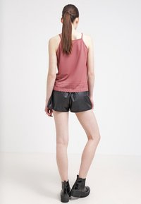 Top in rosa con pizzo, abbinato a pantaloni corti in ecopelle nera e stivali alla caviglia neri chunky. Tessuto liscio, design semplice.