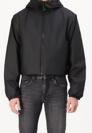 Sort cropped jakke med hætte, frontlynlås, elastiske ærmer og en glat, let tekstur. Parret med mørke denim jeans.