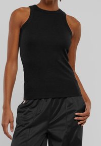 Černý tílkový top z žebrované látky s vysokým límcem a úzkým střihem, kombinovaný s černými sportovními kalhotami. Hladká textura.