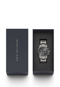 Montre en acier inoxydable argenté avec un cadran gris foncé, présentée dans une boîte bleu marine avec le nom de la marque embossé en or. L'intérieur de la boîte est noir.