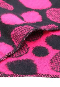 Coperta in lana con grandi pois rosa e neri, che mette in mostra una texture soffice e un punto zigzag lungo il bordo.