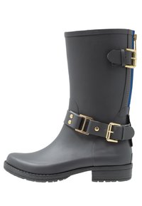 Botín negro de goma hasta el tobillo con acentos de hardware dorado, detalle de hebilla lateral y suela texturizada; cuenta con una cremallera azul en la parte trasera.