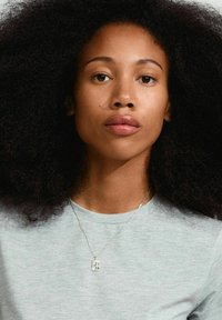 Sølvvedhæng i en halskæde vist på en model med langt, krøllet hår, iført en lys grå T-shirt. Glat tekstur og rektangulær form.