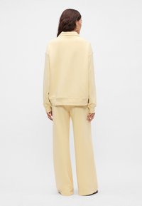 Φούτερ από φλις και χαλαρές παντελόνες σε απαλό κίτρινο. Χαλαρή γραμμή, ριμπ μανσέτες και στρίφωμα. Λείο υλικό χωρίς ορατά σχέδια ή διακοσμητικά στοιχεία.