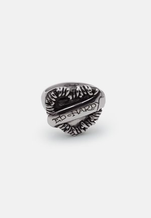 Ασημένιο δαχτυλίδι σε σχήμα καρδιάς με ανάγλυφες λεπτομέρειες φύλλων και χαραγμένη την επιγραφή "Ed Hardy" στο κεντρικό στεφάνι.