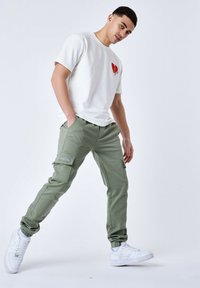 Lett, hvid bomulds T-shirt med et rødt hjerte grafik. Olivengrønne cargo-bukser med sidelommer. Hvide sneakers med teksturerede såler.