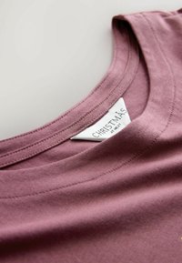 Kortærmet t-shirt med rund hals i mauve, lavet af blødt stof, med et mærke med "JUL" ved halslinjen og glatte syningdetaljer.
