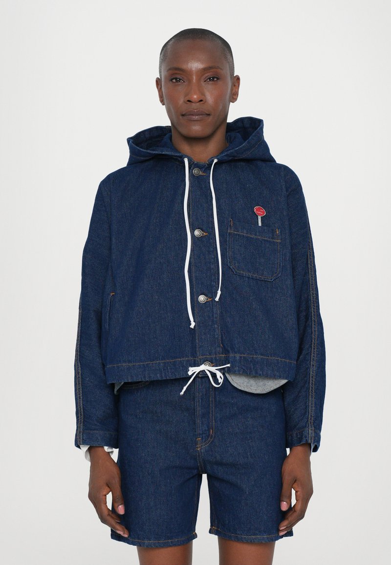 Denim cropped jakke med hætte, med frontknaplukning, hvide snore og en lille rød lap på lommen.