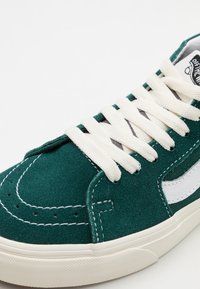 Grüne Wildledersneaker mit weißen Schnürsenkeln, weißer Naht, weißem Seitenstreifen und off-white Gummisohle auf einem weißen Hintergrund.