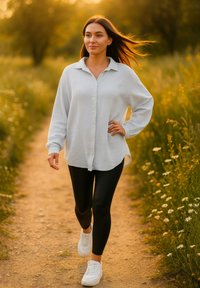 Camicetta grigia chiara con un taglio rilassato e maniche lunghe, abbinata a leggings neri e sneaker bianche, posizionata su un sentiero naturale.