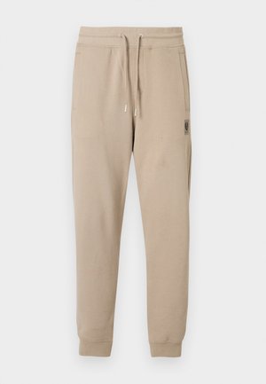 Smėlio spalvos sportinės kelnės iš minkšto medvilnės mišinio, su elastine liemens juosta su raišteliais ir šoninėmis kišenėmis. Mažas logotipo lopas ant klubo.