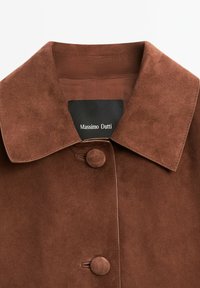 Hnědá semišová bunda s límcem, která má přední zapínání na knoflíky a štítek s nápisem "Massimo Dutti." Hladký povrch, bez viditelných vzorů.