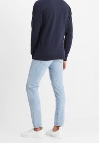 Felpa blu navy con scollo a girocollo, abbinata a jeans azzurri dal taglio dritto. Scarpe da ginnastica bianche completano l'outfit.