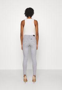 Jeans skinnies grises de cintura alta, con diseño de cinco bolsillos y una etiqueta de marca en la parte posterior. Combinados con una camiseta sin mangas blanca de canalé y tacones nude.