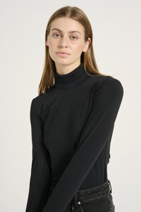 Fekete, hosszú ujjú, álló nyakú felső sima anyagból. Az illeszkedés elegáns, a ujjak testhez simulnak, magas derekú farmernadrággal párosítva.