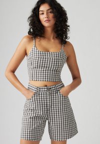 Top scurt cu carouri în negru, alb și maro, asortat cu pantaloni scurți corespunzători. Materialul prezintă un model de tartan constant.