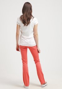 Vit t-shirt med kort ärm, tillsammans med korallfärgade utsvängda byxor. Outfiten har ett mjukt tyg och en enkel design, med subtila detaljer på fickorna.