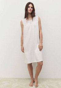 Camicia da notte bianca senza maniche con un yoke testurizzato, delicati dettagli in pizzo e design di lunghezza al ginocchio realizzata in tessuto morbido.