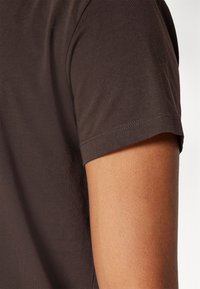 Brun kortermet t-skjorte i myk stoff. Har rund hals, ren søm og en tettsittende design som viser deler av armen.