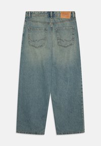 Jeans de denim azul claro con un diseño de pierna recta, que cuentan con un parche de cuero marrón y dos bolsillos traseros con detalles de costura.