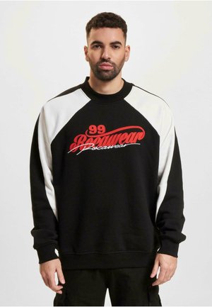 Black sweatshirt with white raglan sleeves, featuring large red embroidered text reading "99 Boomwear." Made of soft fabric with ribbed cuffs.