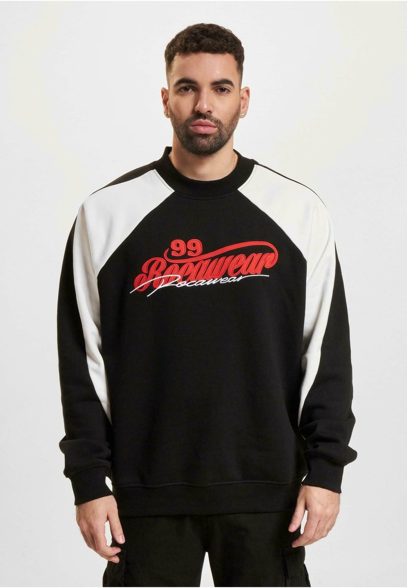 Sweatshirt noir avec manches raglan blanches, arborant un grand texte rouge brodé "99 Boomwear". Fabriqué en tissu doux avec des poignets côtelés.