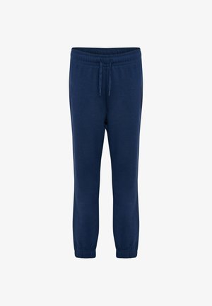 Young boy with curly hair wearing navy hoodie, matching joggers, and blue sneakers, standing against a plain light background.